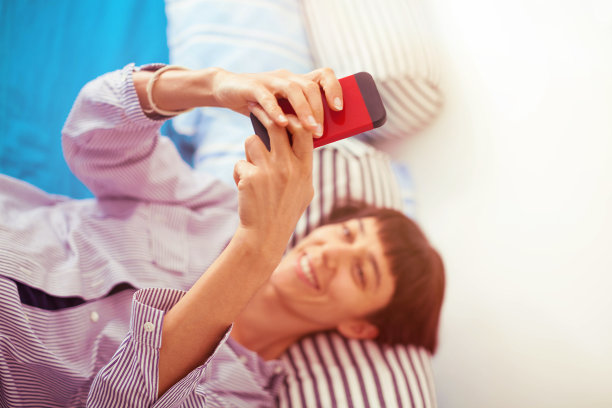 漂亮的年轻女子在床上玩手机图片下载