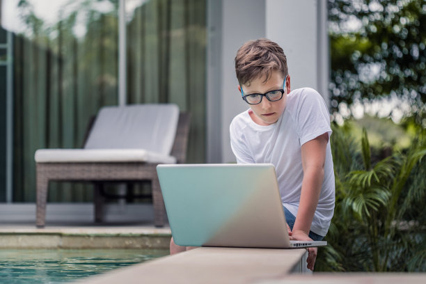 一个男孩坐在泳池边用笔记本电脑图片下载