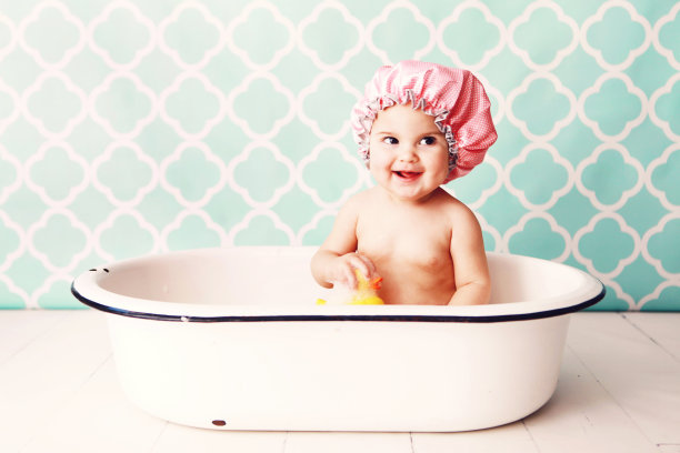 戴着粉色浴帽的宝宝在浴缸里玩橡皮鸭素材图片