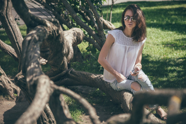 一个拿着智能手机的美女坐在公园里图片下载