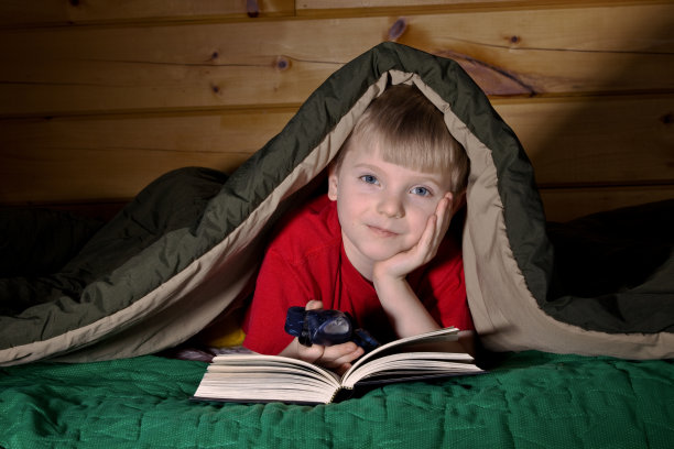 男孩在睡袋下面看书图片下载
