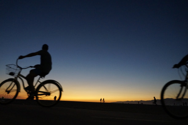 海滩上日落时骑自行车的人的剪影图片下载
