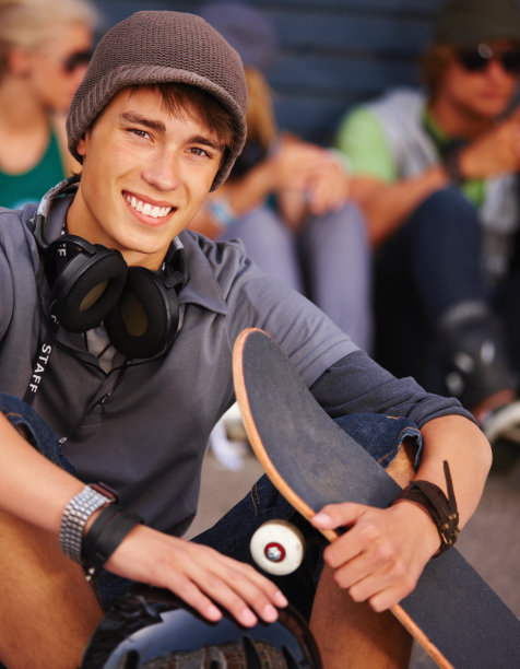 一个十几岁的男孩坐在滑板和微笑的特写图片下载