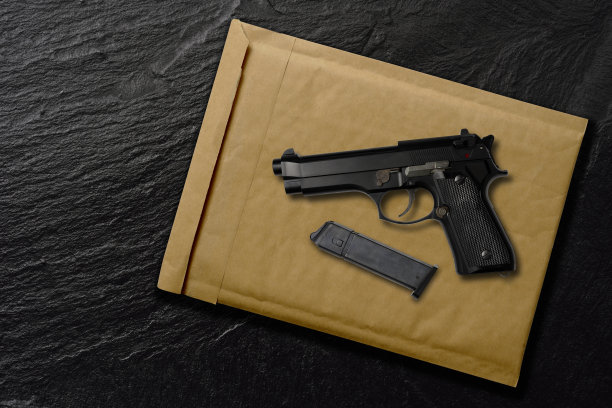 黑色手枪和棕色信封放在闪亮的黑色石头图片下载