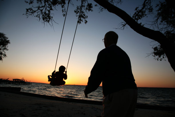 爷爷推着孙子在秋千上玩日落剪影图片下载
