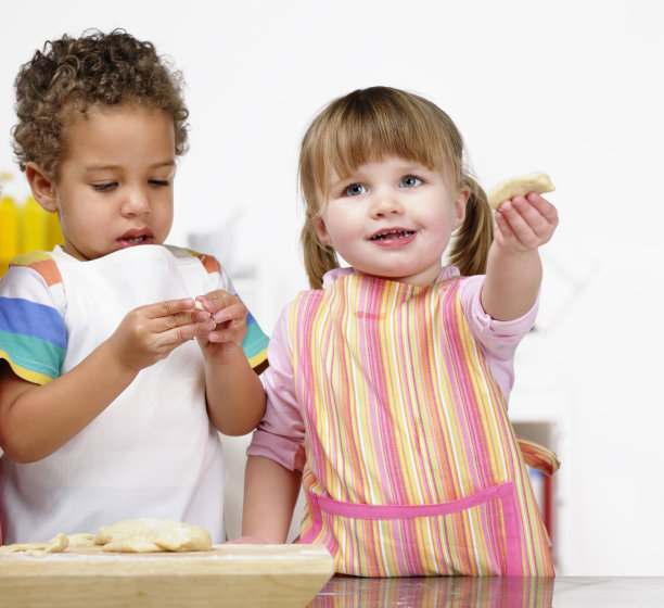 小女孩炫耀准备好的面团，而同行集中注意力图片下载