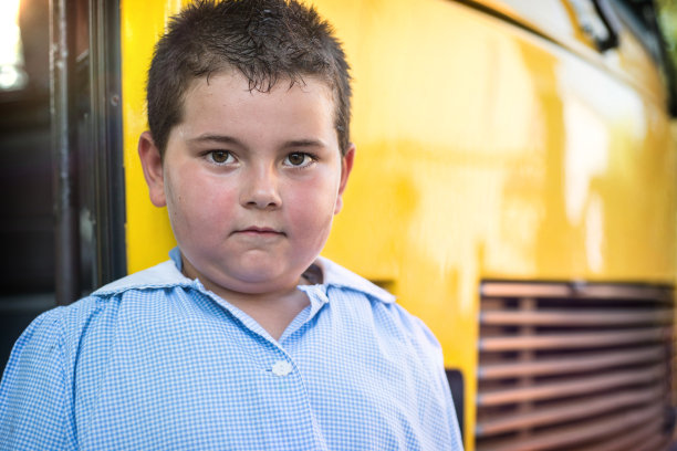 一个5岁的孩子穿着围裙站在一辆校车前面图片下载