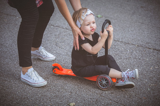 蹒跚学步的小女孩在人行道上骑滑板车。图片下载