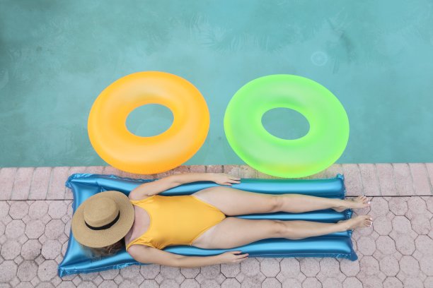 年轻女子躺在游泳池附近，穿着一件泳衣。图片下载