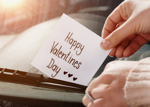 女人的手把“情人节快乐”的纸条塞在挡风玻璃的雨刷下素材图片