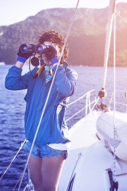 年轻女子驾船，用双筒望远镜看图片下载