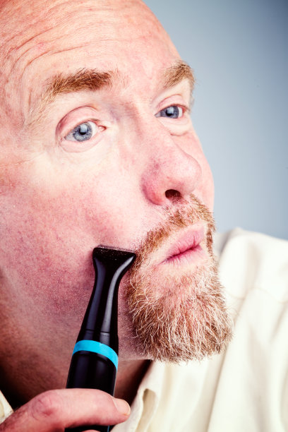 成熟的大胡子男人用电动定时器塑造小胡子图片下载