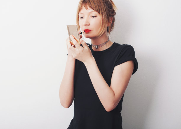 女孩在化妆，画着嘴唇，看着镜子。图片下载