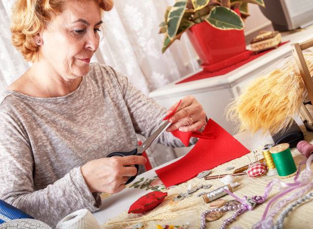年长的妇女正在用剪刀剪红色的织物图片下载