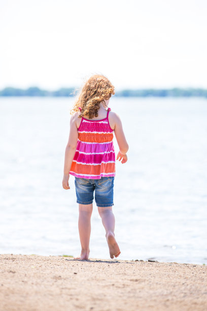 后视图的女孩走向水的边缘在海滩图片下载