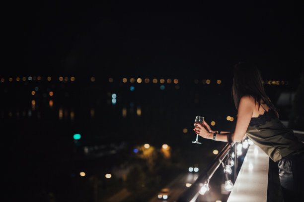 漂亮的年轻女子靠在阳台的篱笆上图片下载