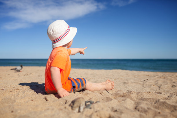 小男孩坐在海滩上，指着大海图片下载