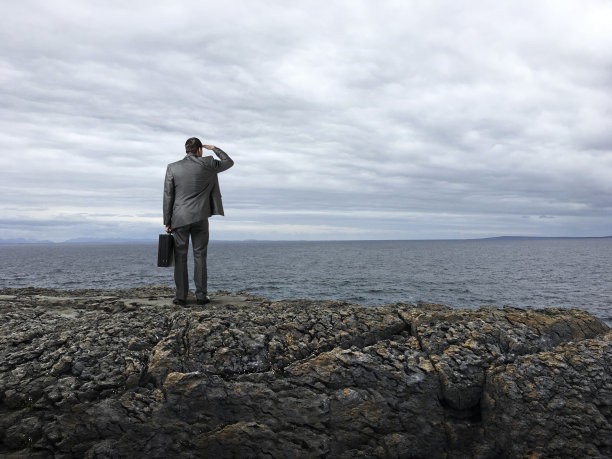 商人站在悬崖上俯瞰着不祥的天空和汹涌的大海图片下载