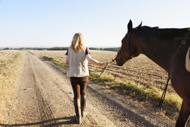 一个成熟的女人牵着她的马走在乡间小路上图片下载