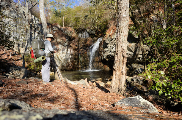 一个背着背包的男人站在瀑布附近的树林里图片下载