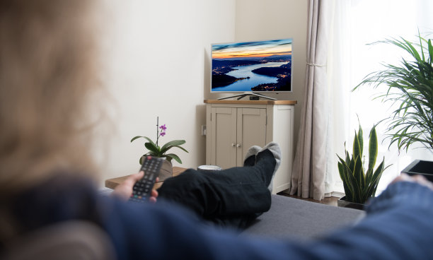 女人坐在沙发上，手里拿着遥控器，在家里的客厅里看电视图片下载