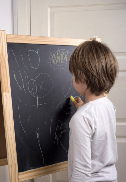 小男孩用粉笔在黑板上画画图片下载