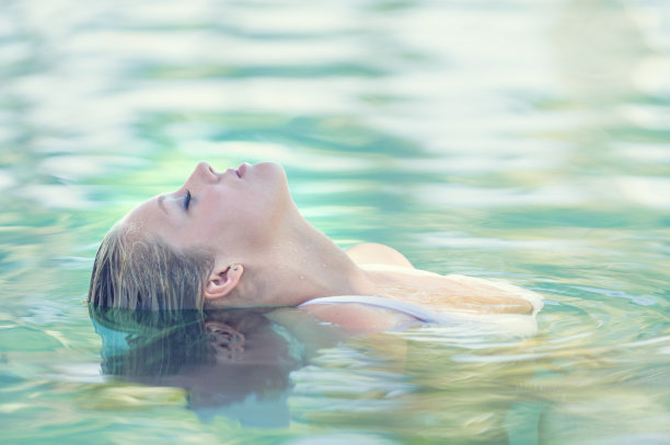 美丽的女人漂浮在绿松石游泳池图片下载