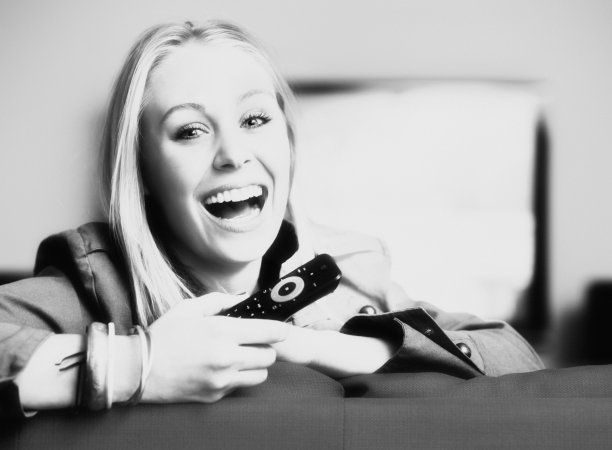 金发美女拿着电视遥控器笑得很开心。黑白照片图片下载
