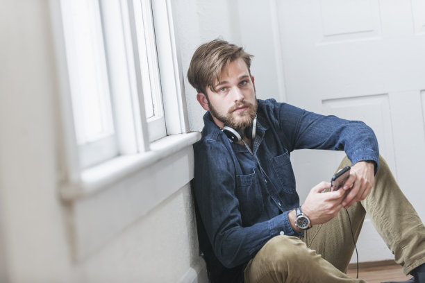 年轻人坐在地板上，戴着耳机，拿着电话图片下载