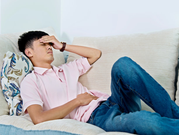 一个年轻的亚洲男人躺在沙发上，痛苦不堪图片下载