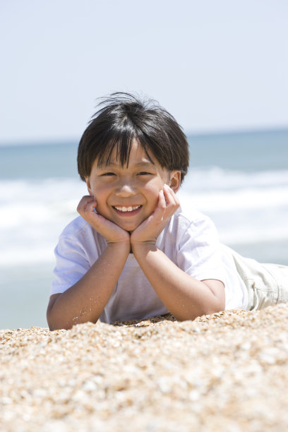 快乐的亚洲男孩躺在沙滩上图片下载