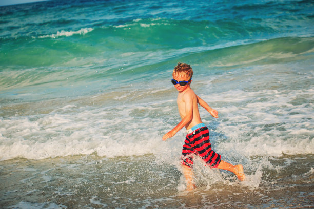 快乐的小男孩在海滩上跑着玩海浪图片下载