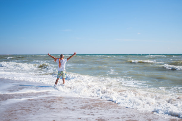 快乐的人站在海滩冲浪线，伸开双臂图片下载