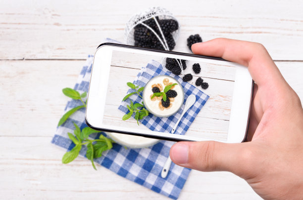 手拍照片酸奶与麦片和黑莓与智能手机。图片下载