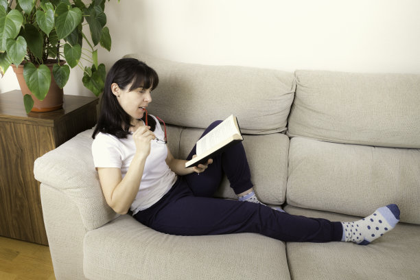 一个戴眼镜的女人在沙发上看书图片下载