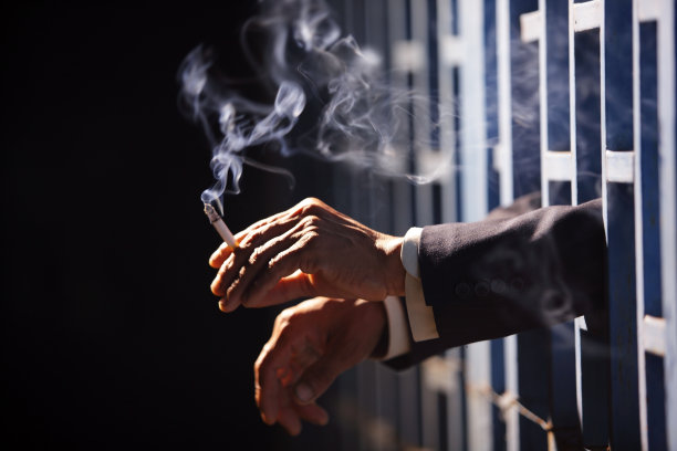 黑色背景的监狱里，一个商人的手在抽烟。图片下载