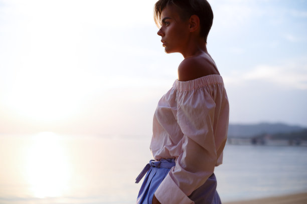 美丽的女模特穿着粉红色的衬衫和蓝色的短裤在海边摆姿势图片下载