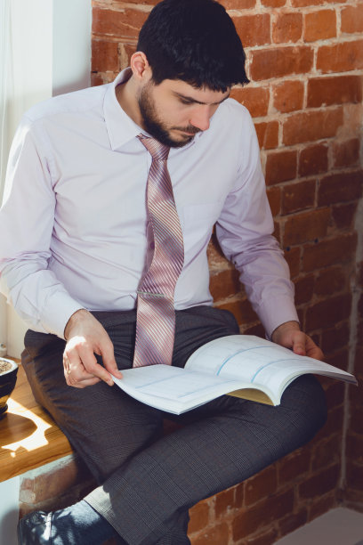 一个年轻人在办公室的窗口看杂志。图片下载