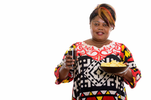 一名超重的非洲黑人妇女面带微笑，手里拿着一碗薯片和一杯汽水图片下载