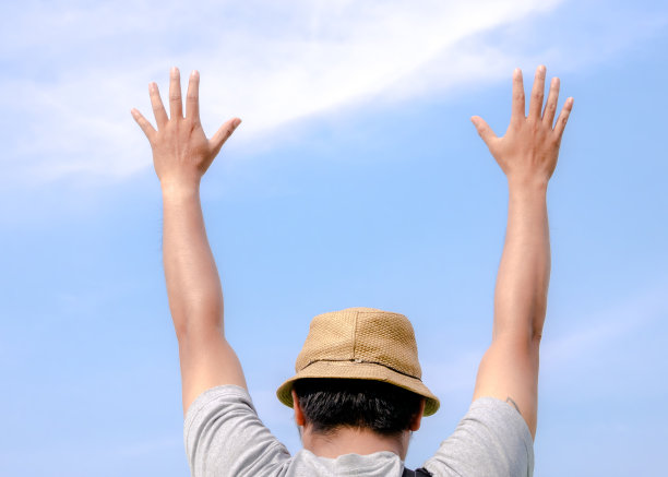男人开心的举起双手双手掌心，小伙子休闲的穿在蓝天的背景上图片下载