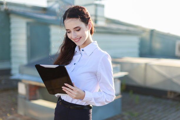 漂亮的女商人穿着白衬衫黑裙子站在屋顶上拿着平板电脑图片下载