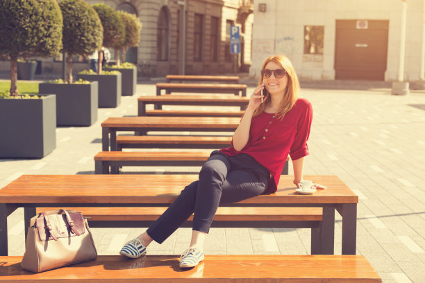 时尚可爱的女孩喝咖啡和使用她的手机在户外。图片下载