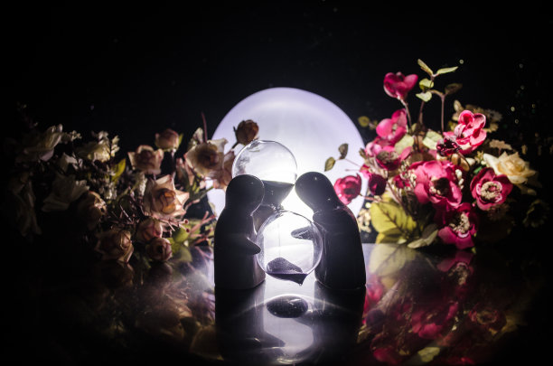 两个娃娃抱在有花和月亮装饰的桌子上，灯光背景有烟。爱的概念。贺卡或礼品卡的设计理念。复古的基调。情侣拥抱剪影图片下载