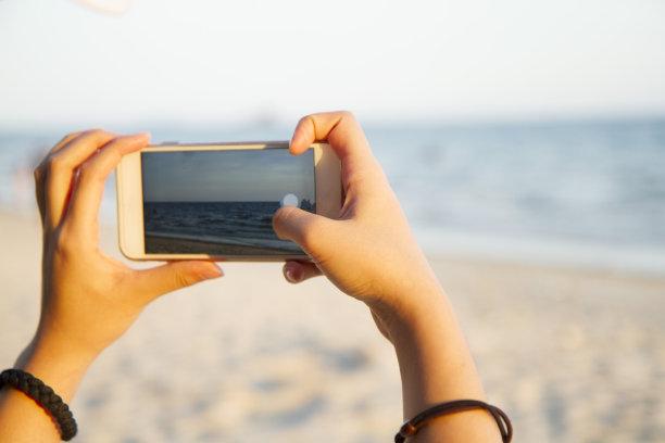 一名女子用智能手机拍摄海滩风景图片下载