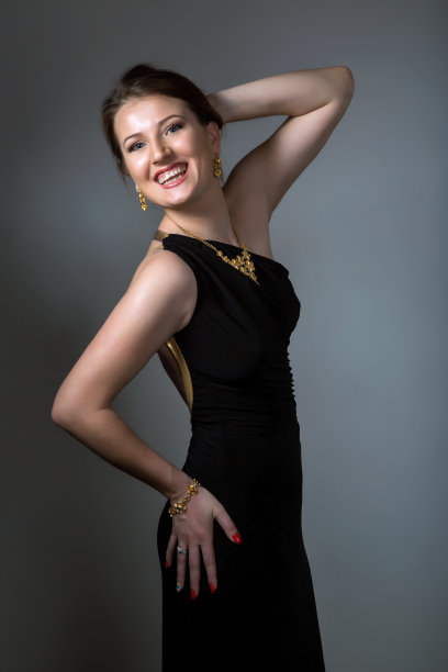 年轻的黑发女士在黑色裙子摆姿势在深灰色的背景。工作室拍摄，垂直图像图片图片下载