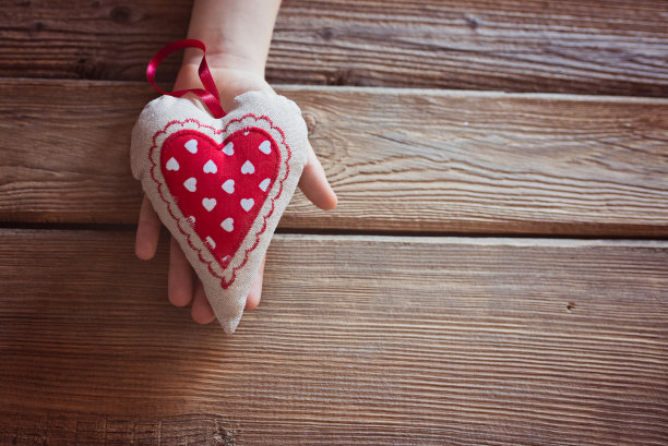 孩子手里拿着红色的纺织心在一张木桌上。图片下载