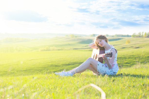 美丽的年轻女子在日落时弹吉他图片下载