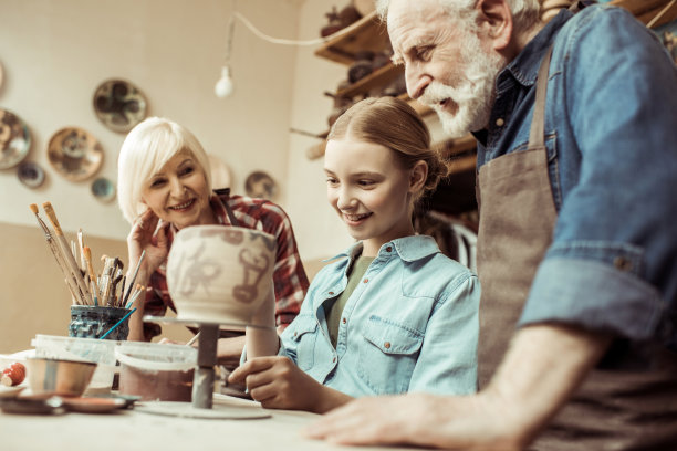 正面的女孩画陶罐和祖父母帮助在车间图片下载