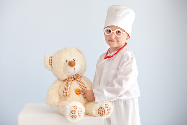 穿着医疗袍的孩子正在对待玩具熊。婴儿的医生图片下载