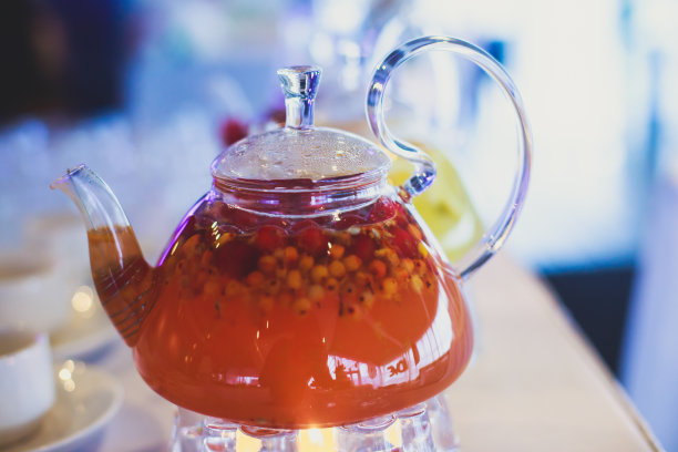 美丽温暖的图片透明茶壶茶壶与可口的红茶与苹果，柠檬和姜在桌子上蜡烛和甜点的背景图片下载